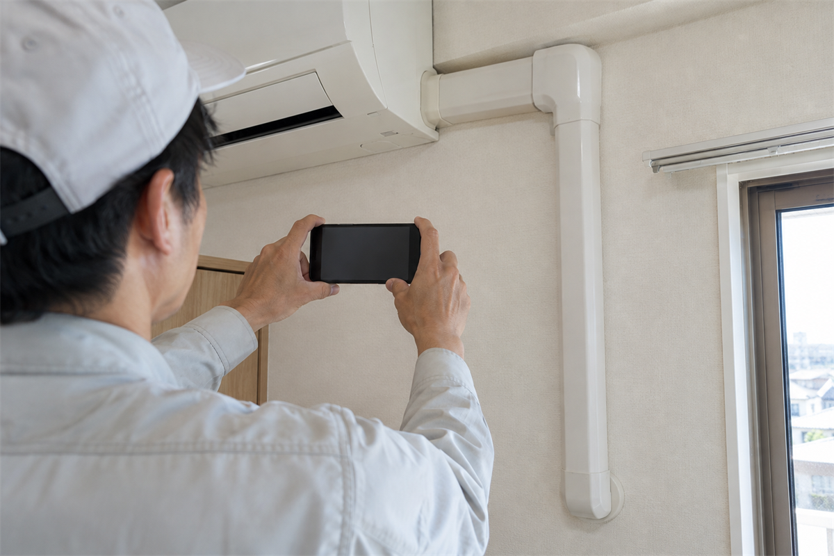 室内の配管化粧カバーをスマートフォンで撮影する施工者