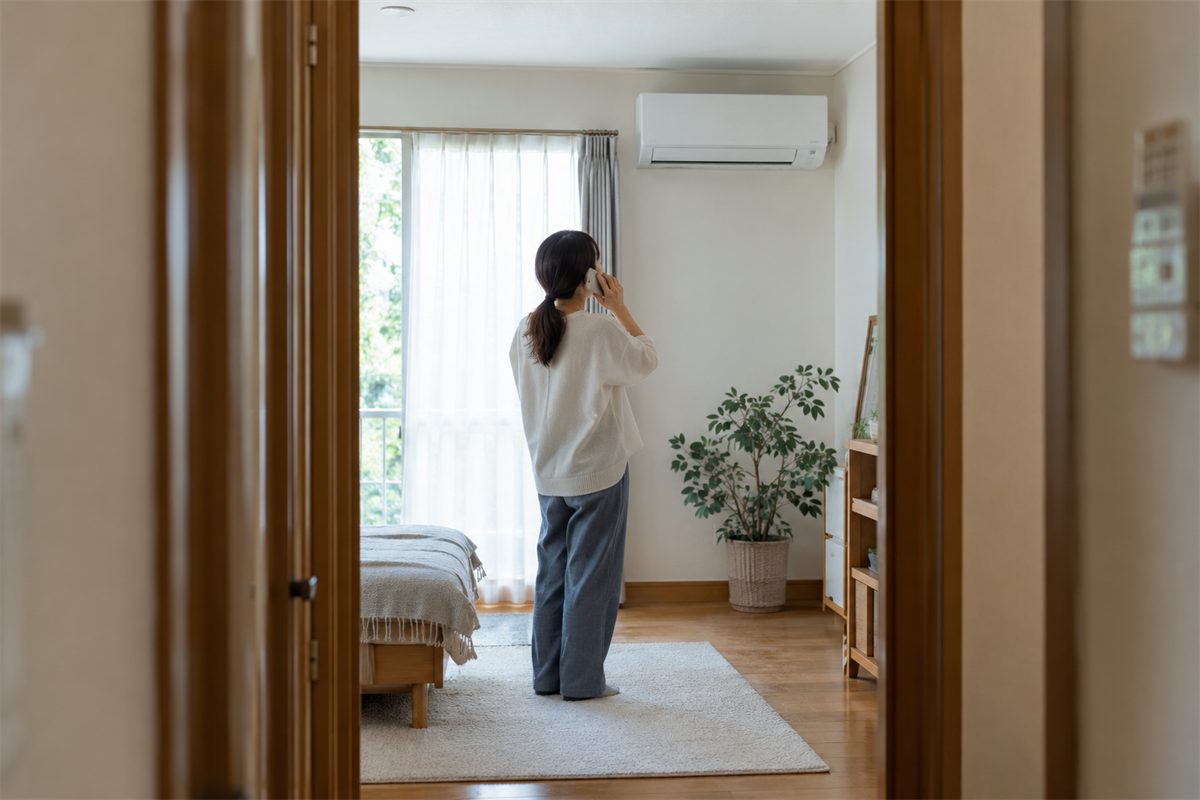 室内機から離れた場所で施工店へ電話相談する住人